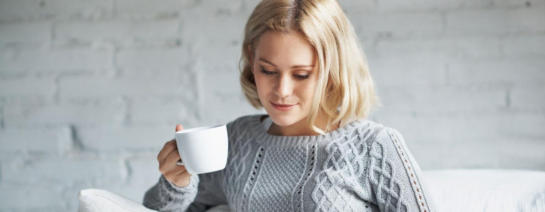 a woman sits on a couch with a cup of coffee and looks at her tablet