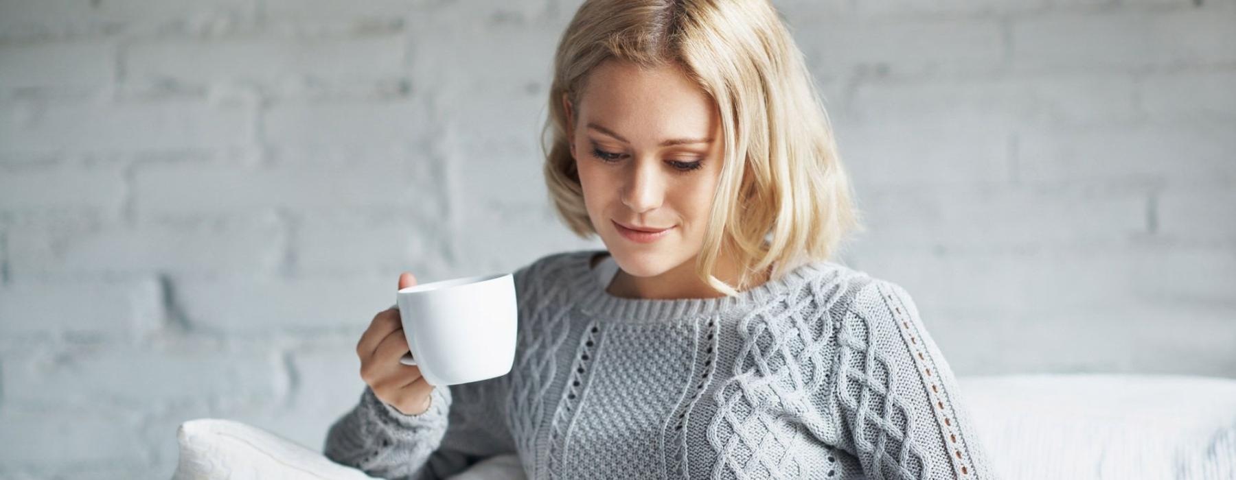 a woman sits on a couch with a cup of coffee and looks at her tablet